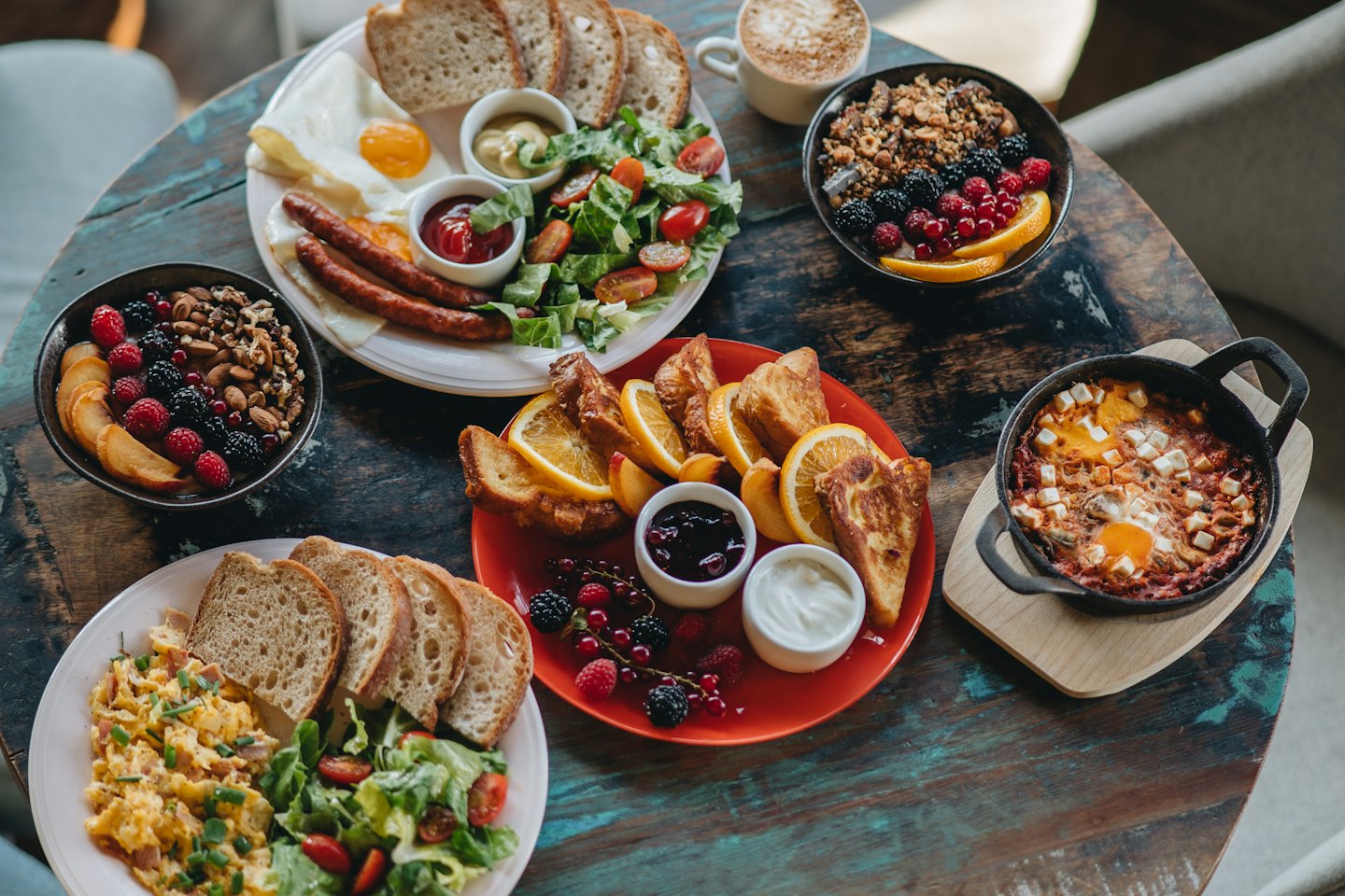 Abundant breakfast spread with eggs, sausages, and fruit on a wooden table.