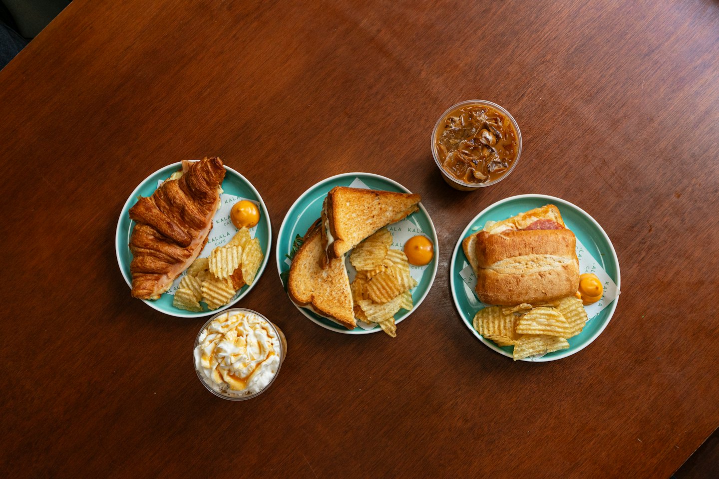 Assorted sandwiches and iced drinks arranged on wooden cafe table.