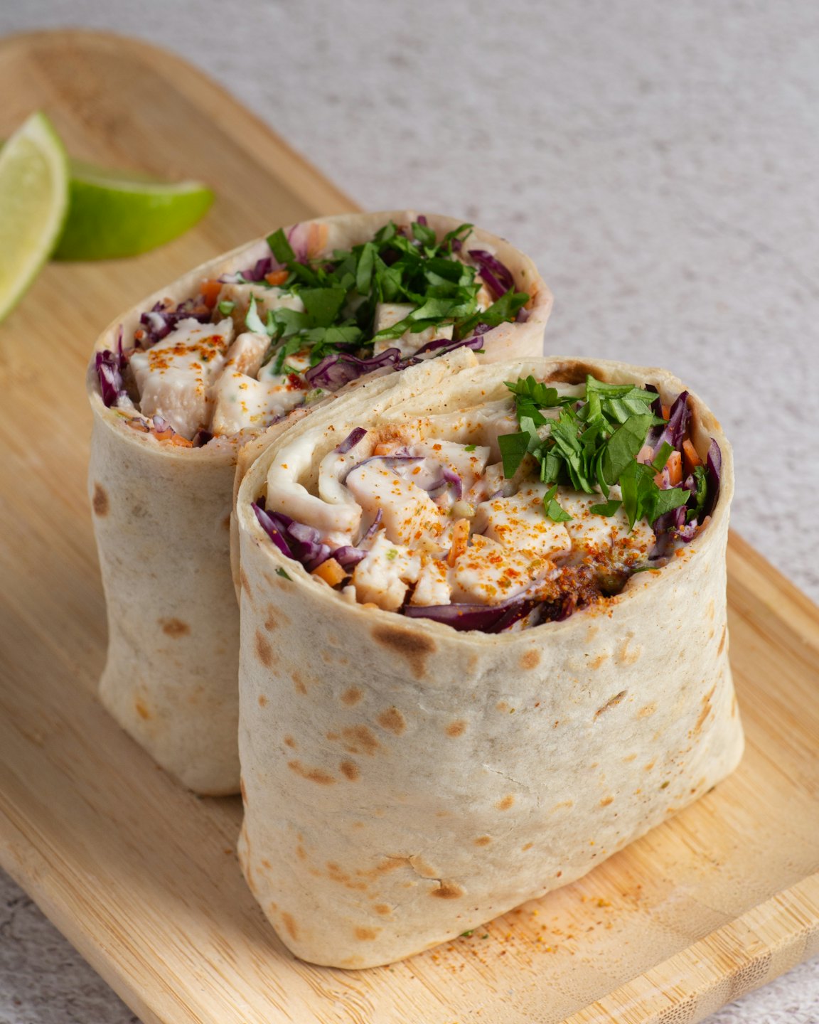 Two fresh food wraps with meat and vegetables on a cutting board.