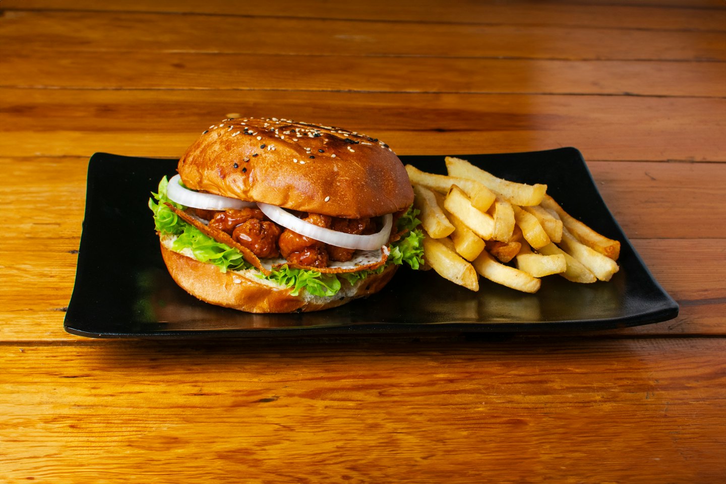 Gourmet fried chicken burger and fries on a black plate.