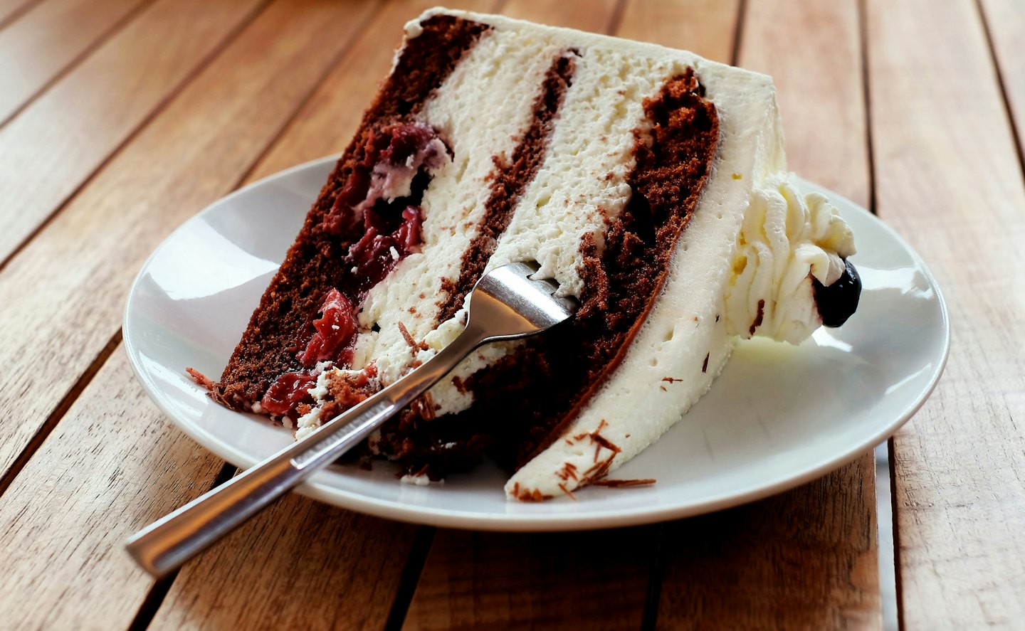 Slice of layered chocolate cake with cream and cherry filling on a plate.