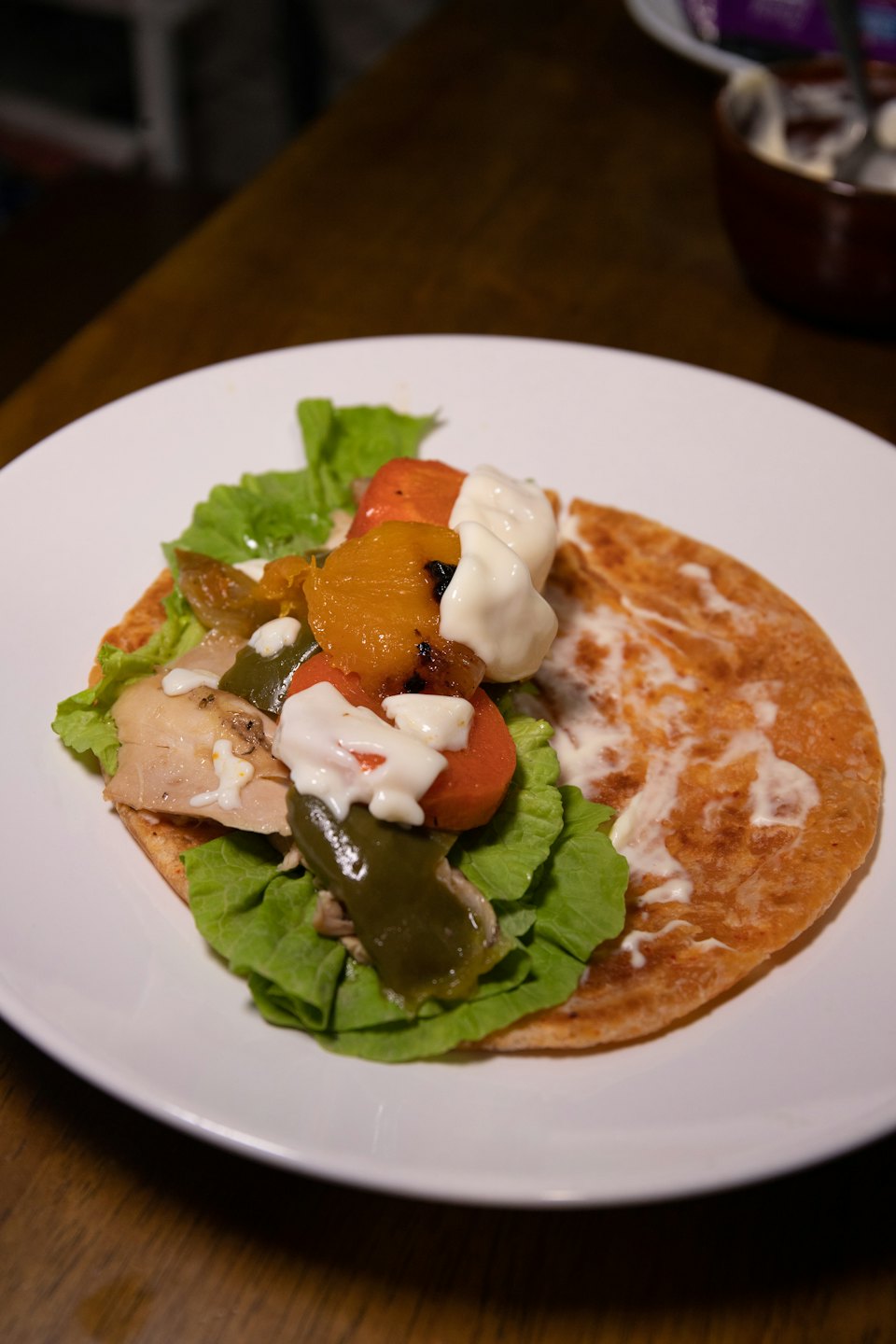 Chicken and vegetable tortilla wrap with creamy sauce on a plate.