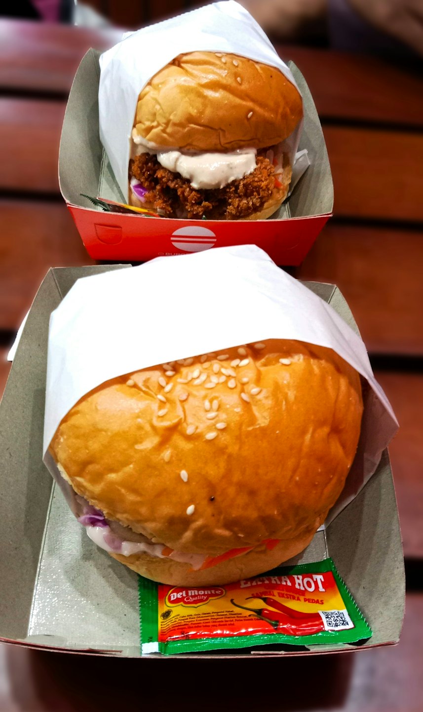 Two delicious burgers in takeaway boxes on a wooden table.